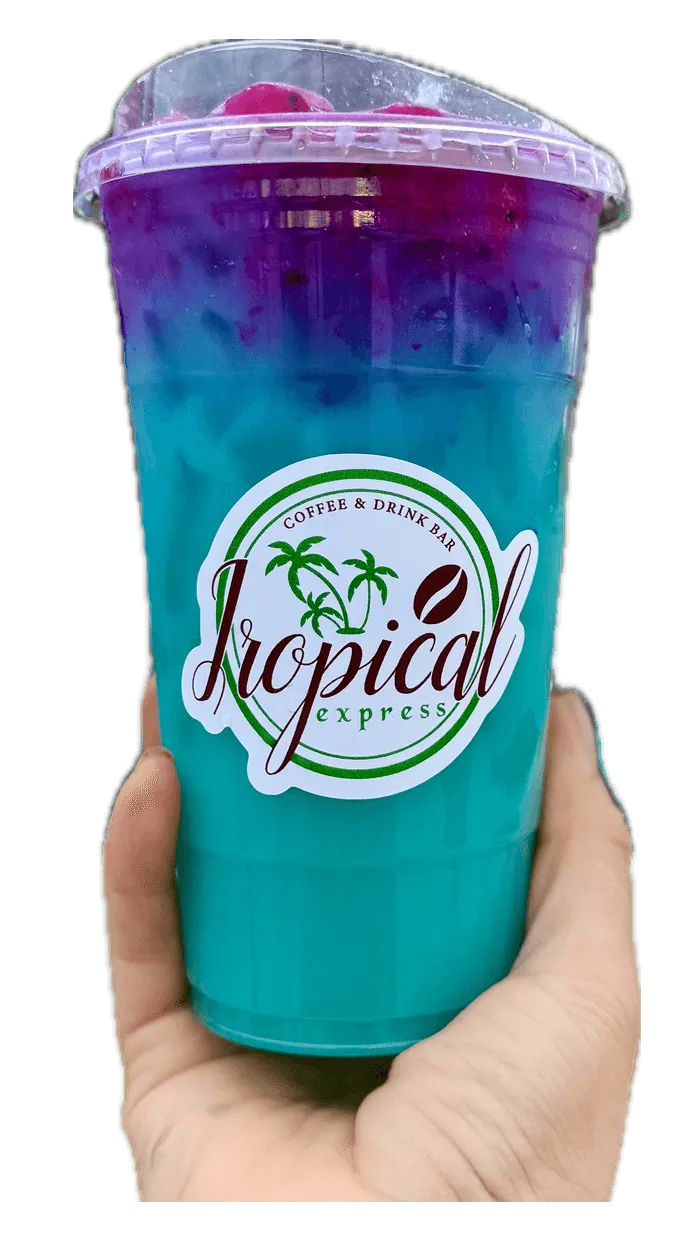 A hand holding a Tropical Express cup of Dragon Frost — an icy blue curaçao, vanilla and white peach drink with coconut milk topped with dragon fruit