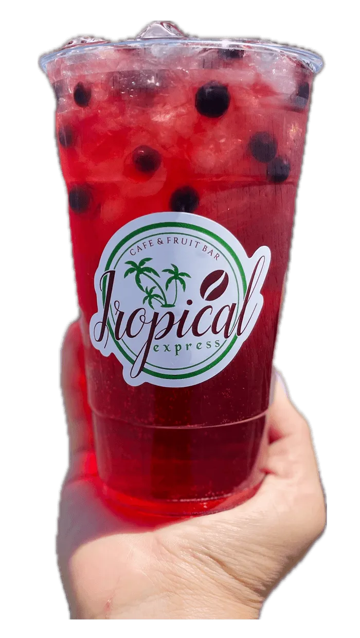 A hand holding a Tropical Express cup of Island Punch — a red cherry, white peach and blueberry drink topped with fruit