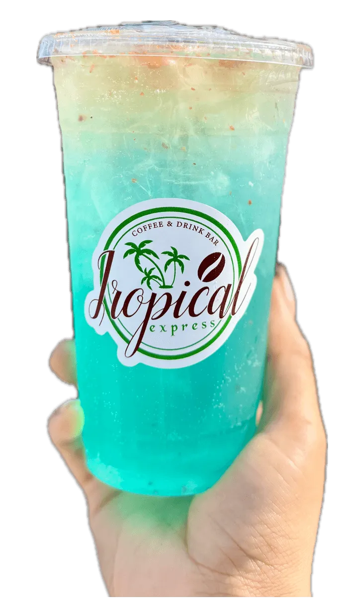 A hand holding a Tropical Express cup of Pacific Heat — a lime-green LOTUS energy drink with lemon, cucumber and lime dusted with Tajín