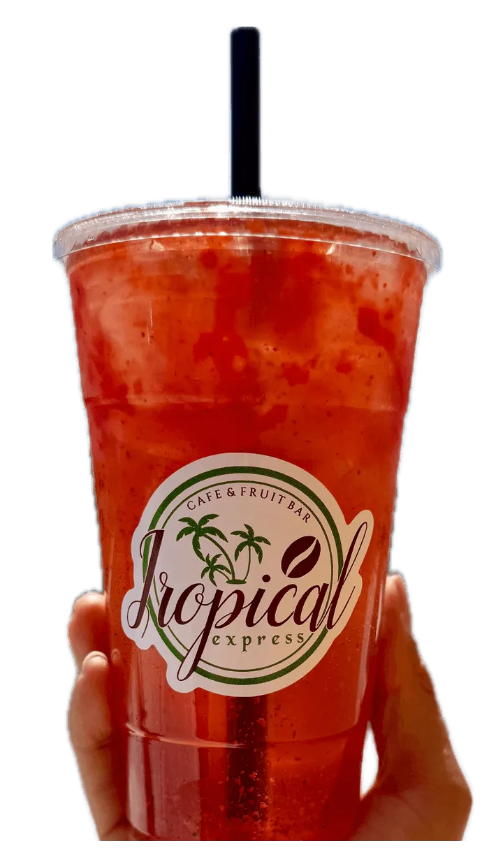 A hand holding a Tropical Express cup of Sunset Breeze — a red-orange grapefruit, passion fruit and guava refresher with Tajín and chamoy